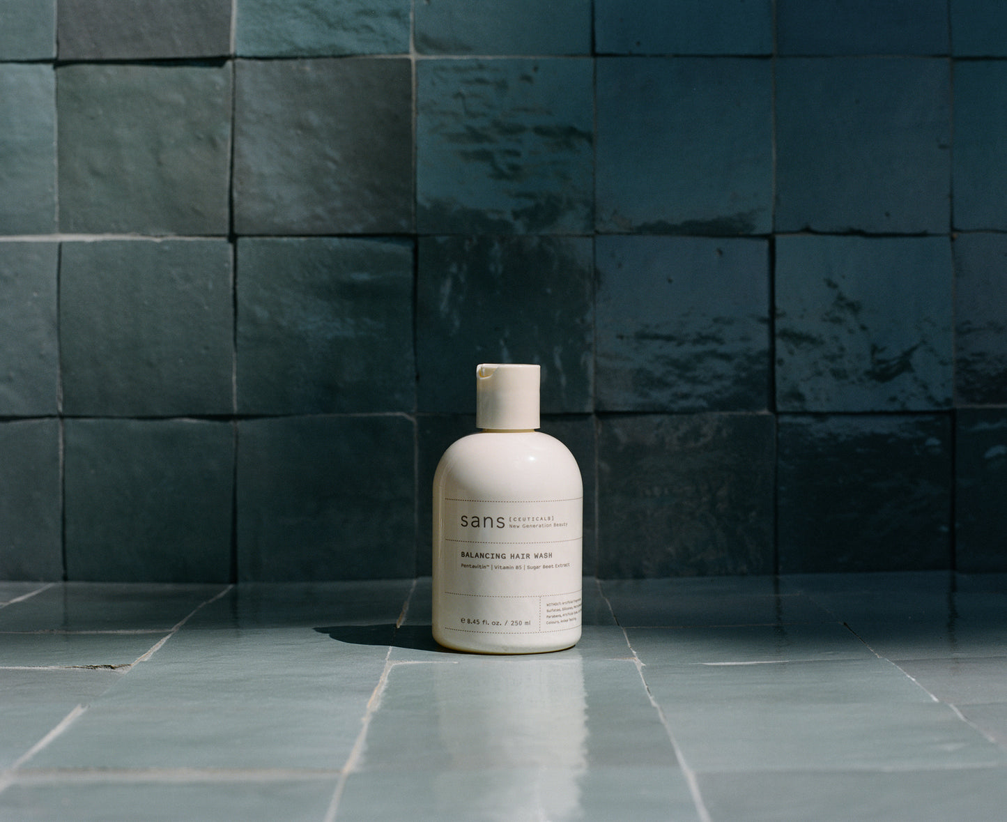 Bottle of 'sans' product on a tiled floor with dark blue tiles in the background