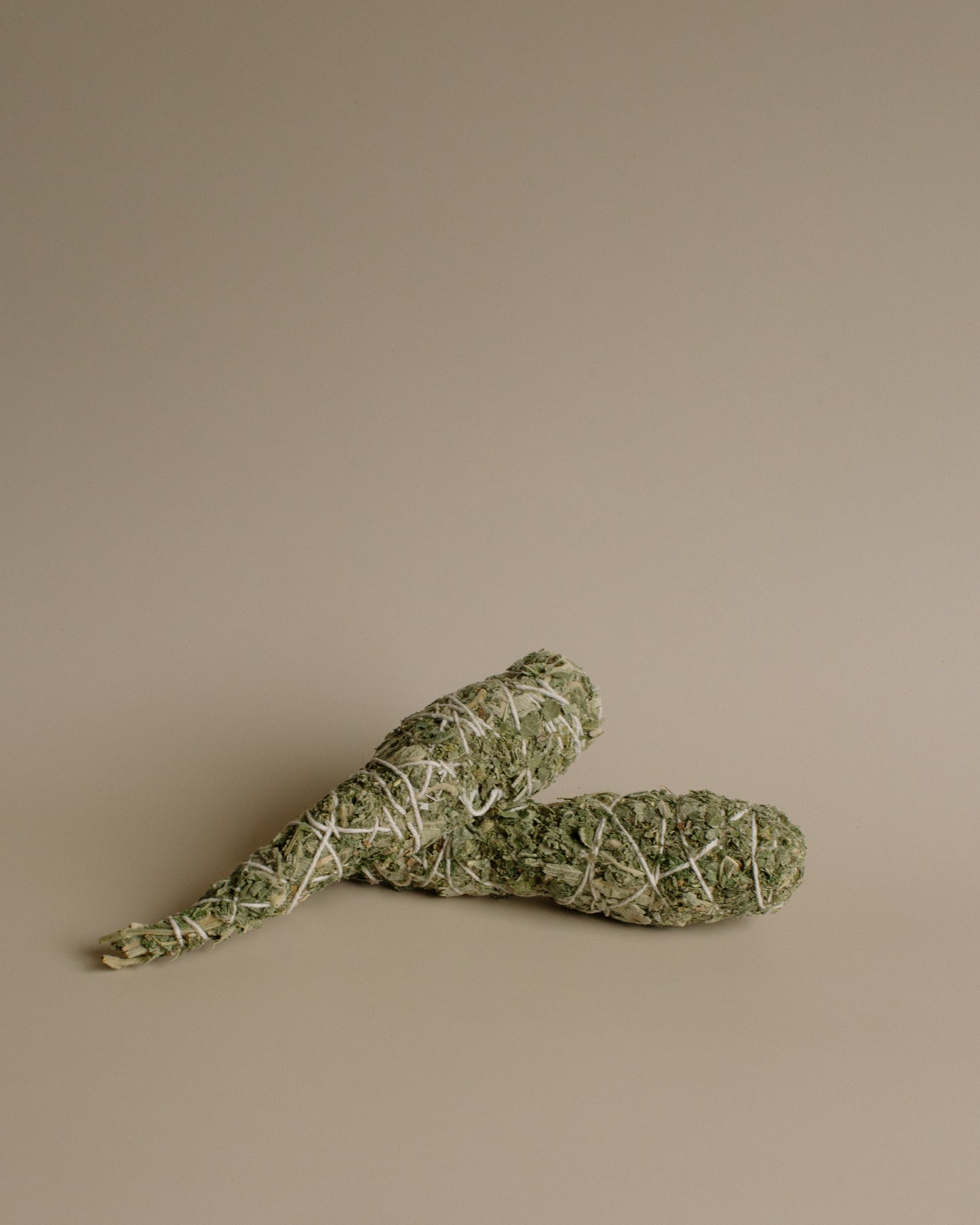 Two sage smudge sticks on a beige background