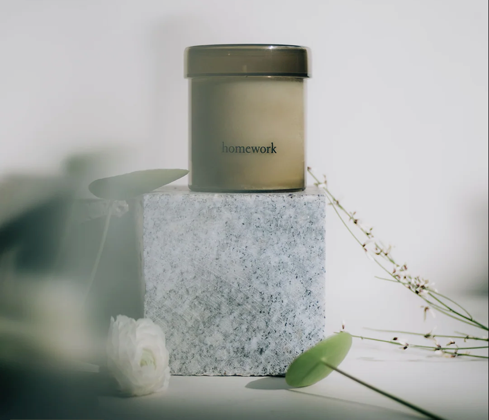 Candle labeled 'homework' on a textured block with flowers and leaves in the background