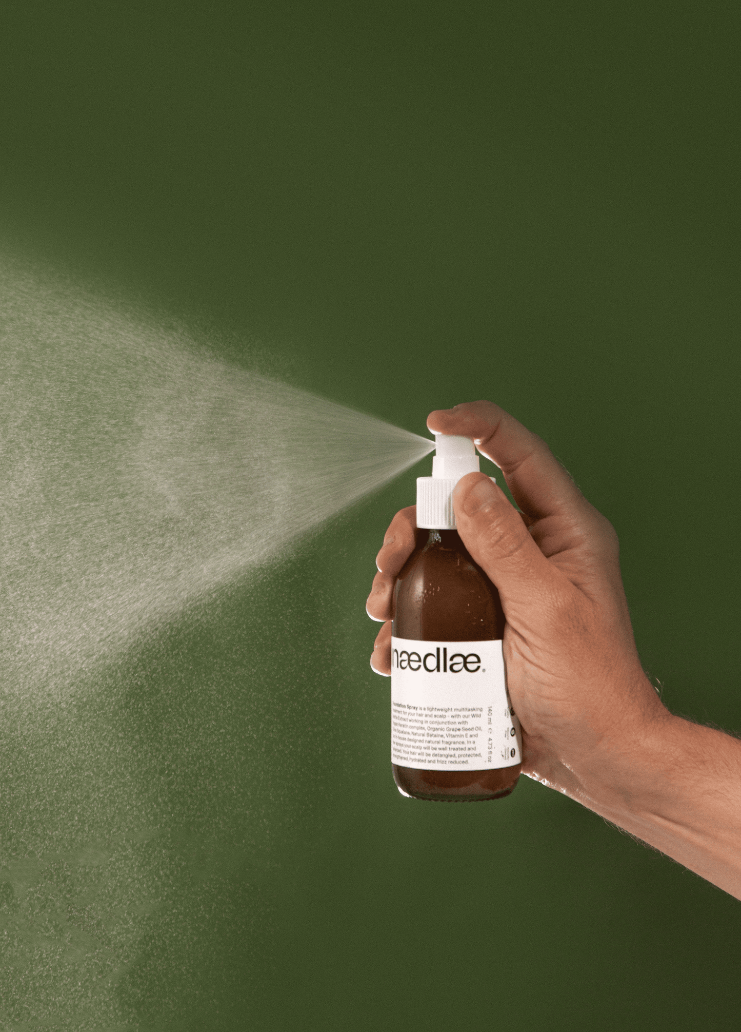 Hand holding a brown spray bottle labeled 'Naedlae' against a green background