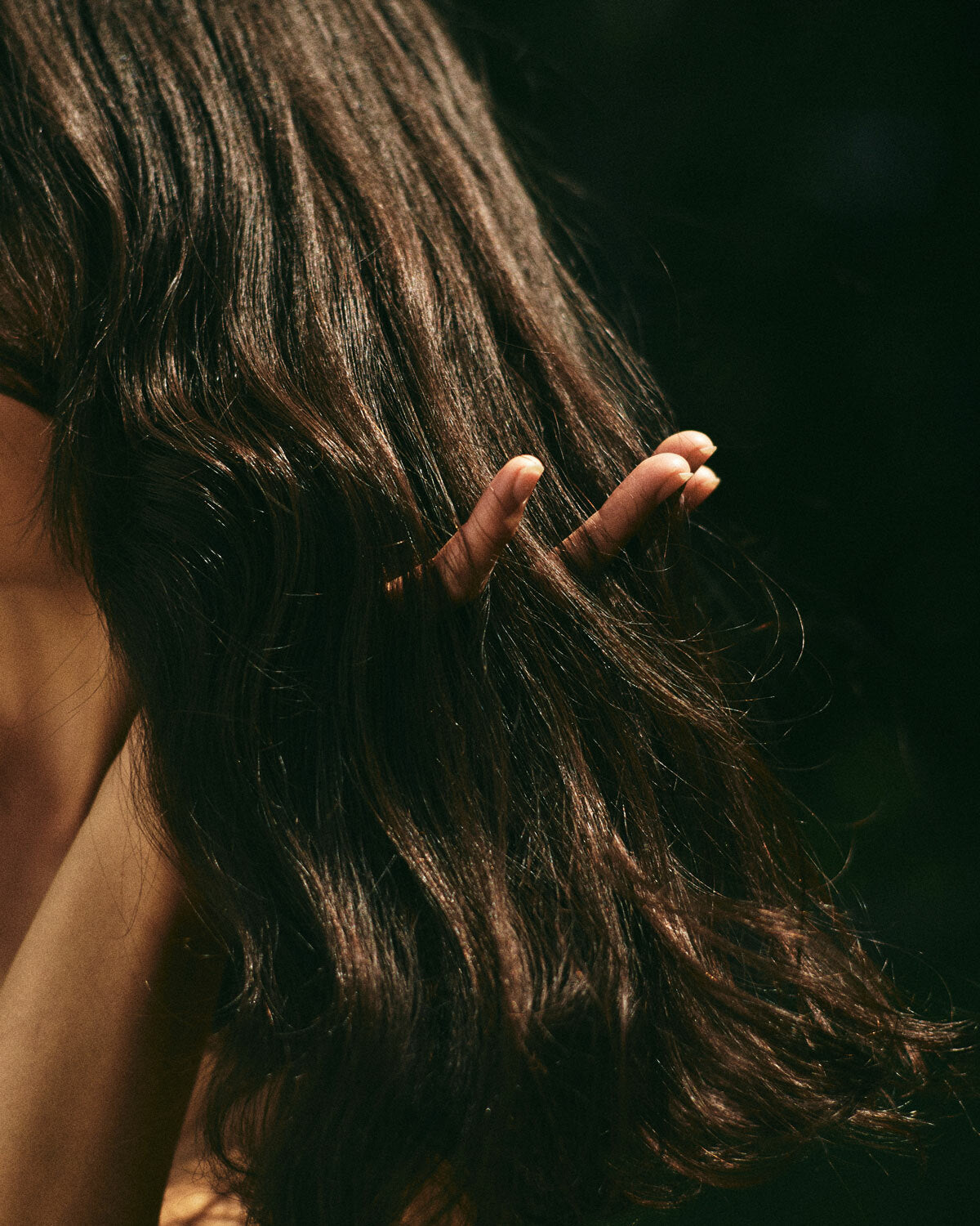 Close-up of a person holding their long, wavy hair with a dark background