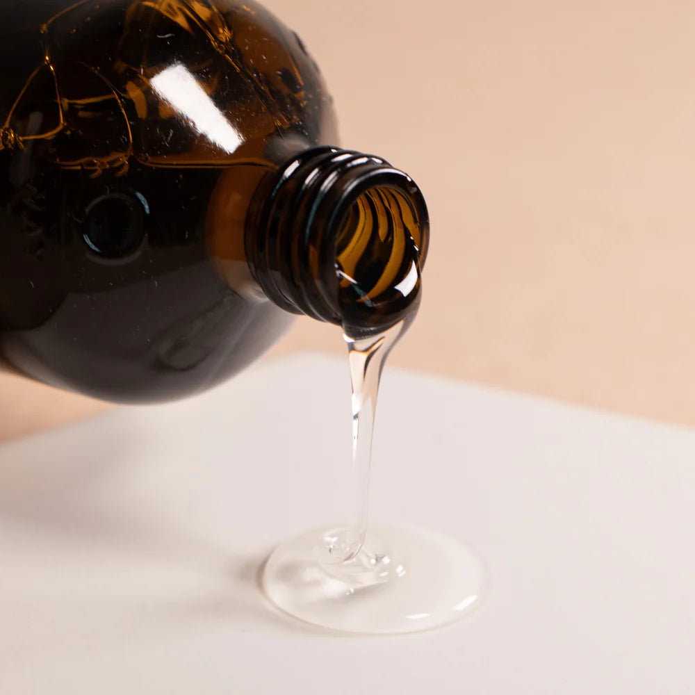 Brown bottle pouring liquid onto a flat surface creating a puddle of product