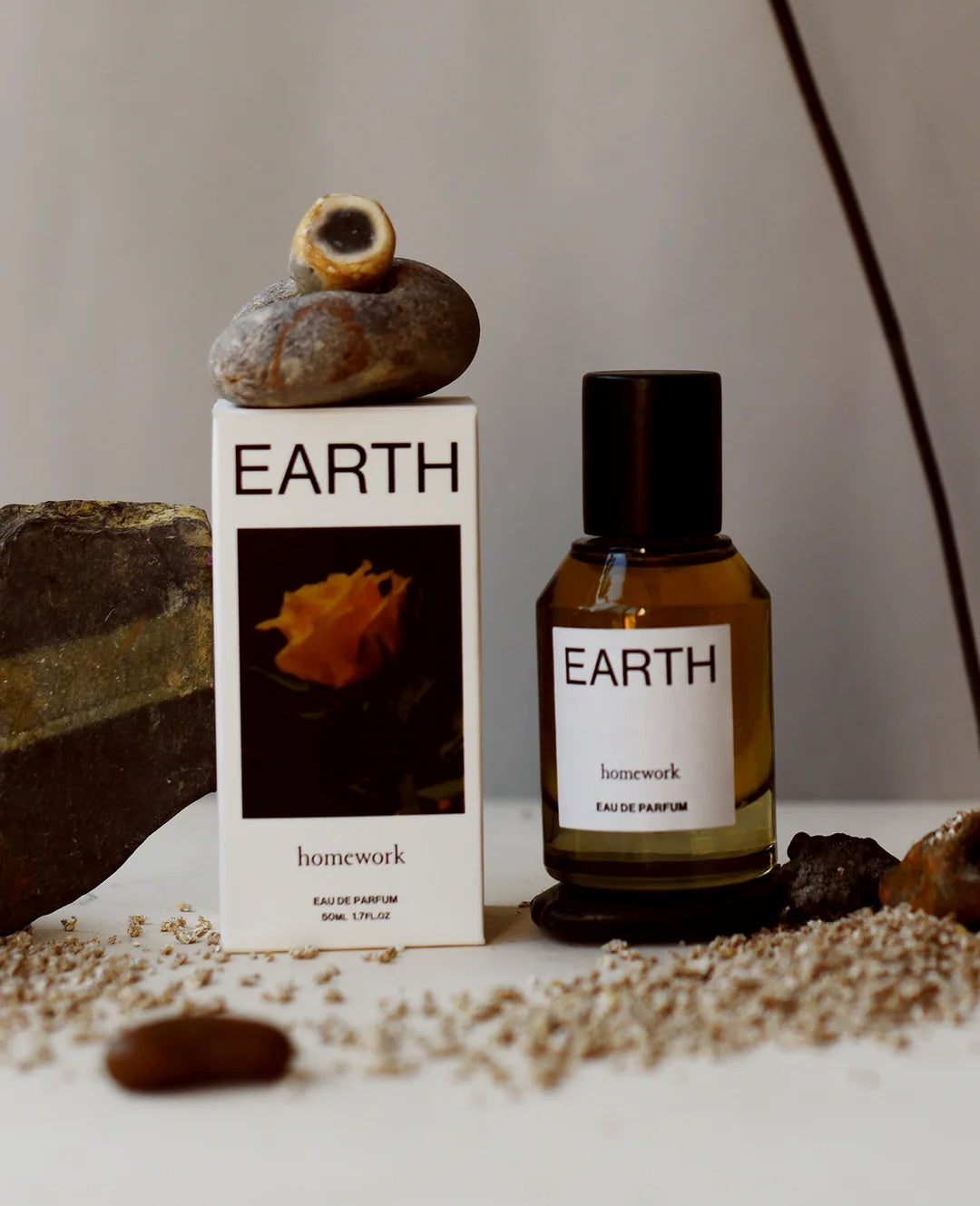 Earth-themed perfume bottle and packaging on a neutral background with rocks and seeds.