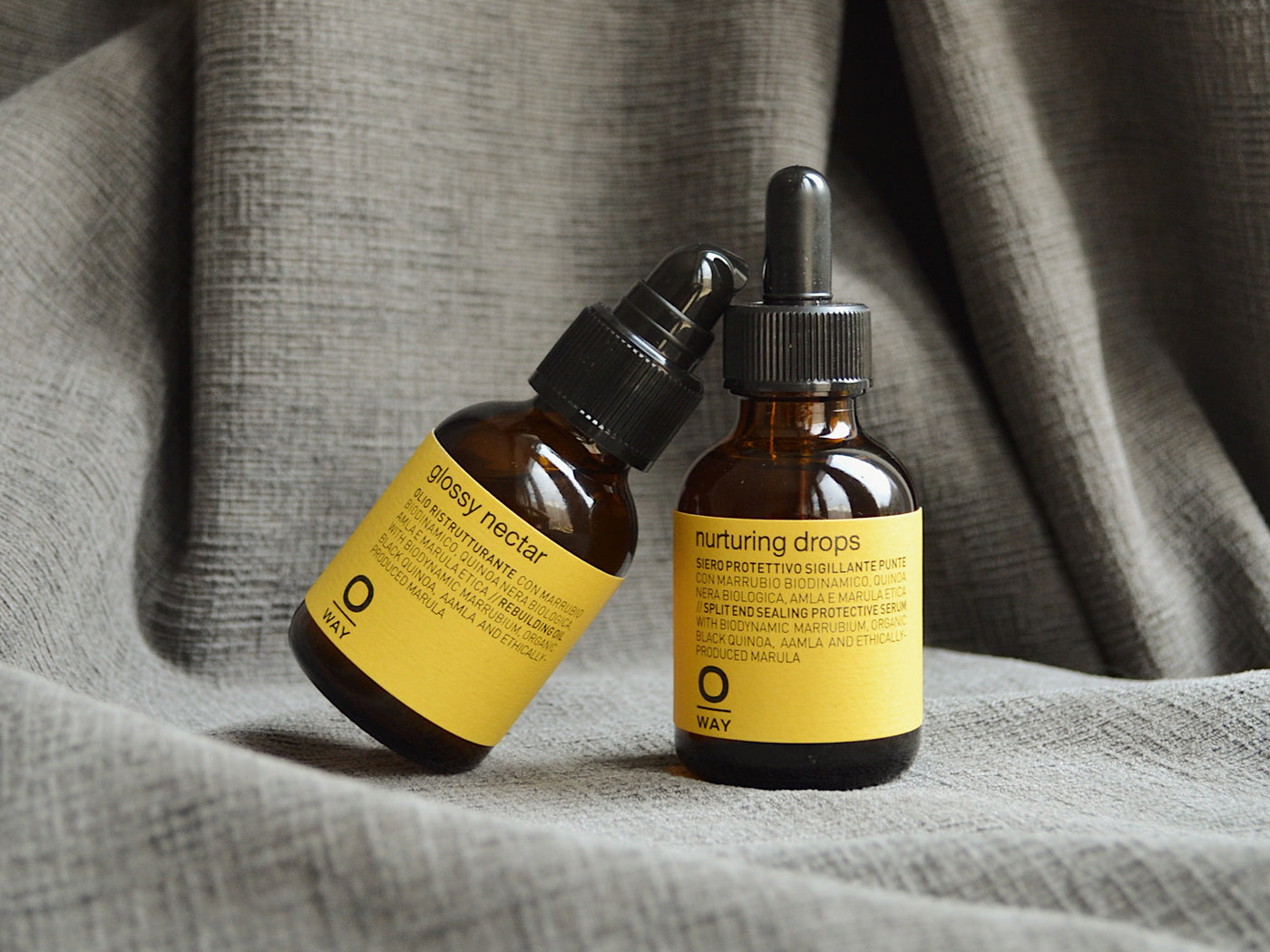 two small pipet bottles with yellow label on grey textured fabric background