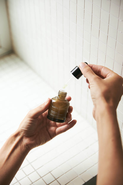 Person holding a dropper bottle with a white tiled wall in the background