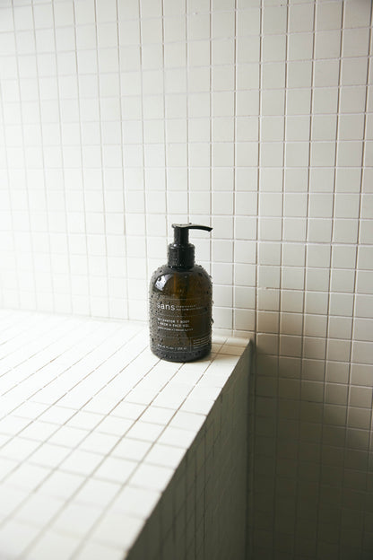 A dark-labeled bottle with a pump dispenser on a tiled bathroom shelf
