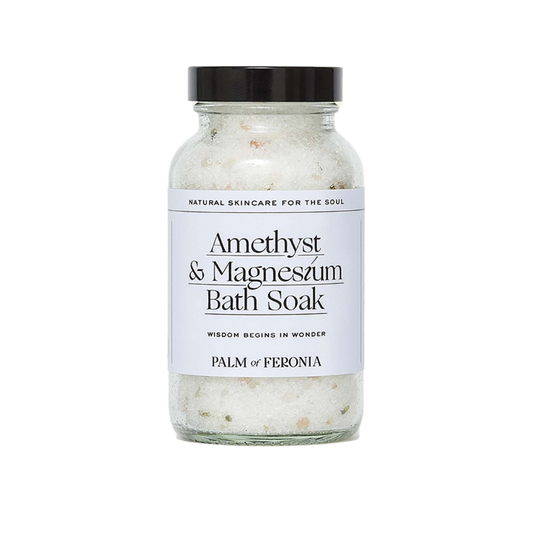 A clear glass jar containing white bath soak with a label that reads 'Amethyst & Magnesium Bath Soak' and the brand name 'Palm of Feronia'. The jar has a black lid and is labeled as a 'Natural Skincare Product for the Soul'.