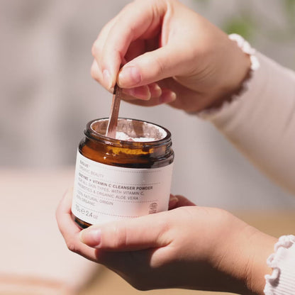 Hands holding small jar of light pink facial powder cleanser