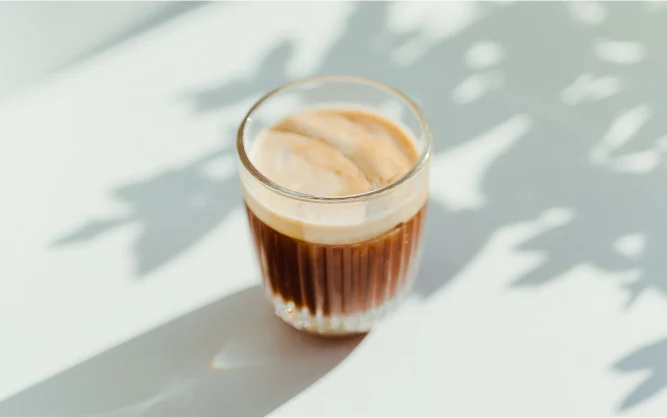 Glass of iced coffee on a light surface with shadows