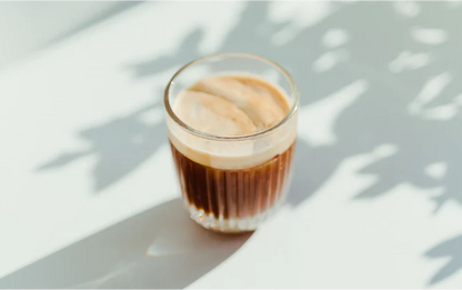 Glass of iced coffee on a light surface with shadows