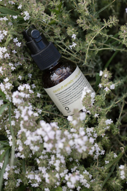 Bottle of Oway Dandruff Remedy surrounded by white flowers and green leaves