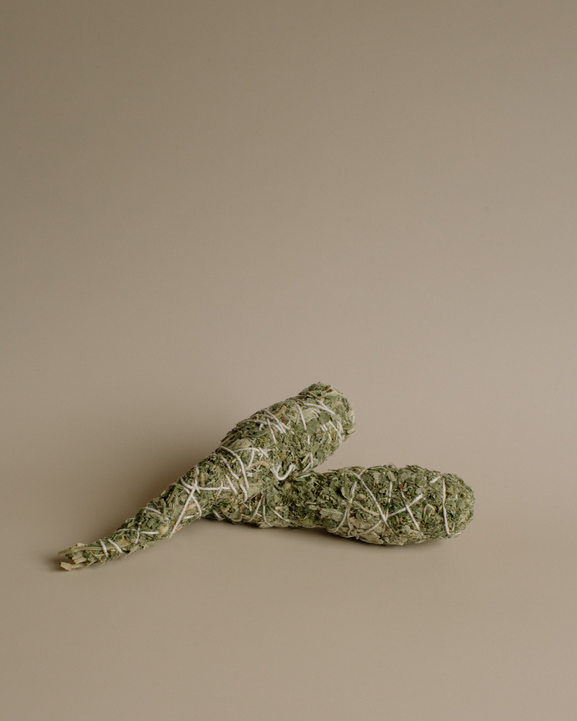 Two sage smudge sticks on a beige background