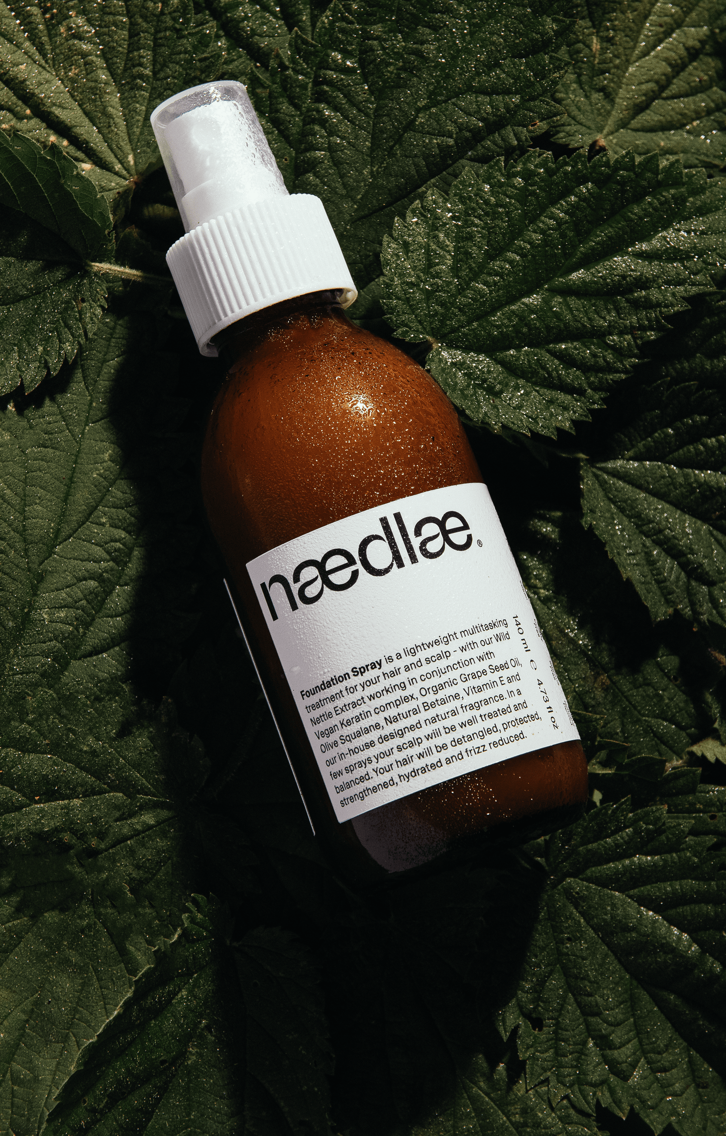 Brown bottle of hair product with white label on a bed of nettle leaves
