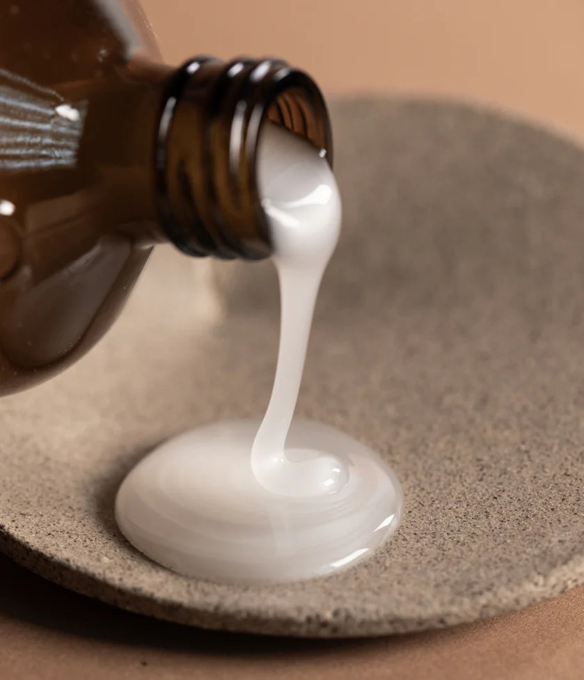 White liquid being poured from a brown bottle onto a textured surface