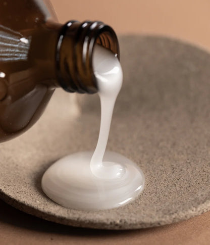 White liquid being poured from a brown bottle onto a textured surface