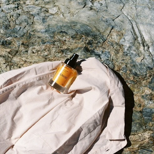 Bottle of Rowse Summer Mist placed on a beige cotton jacket on a textured stone surface