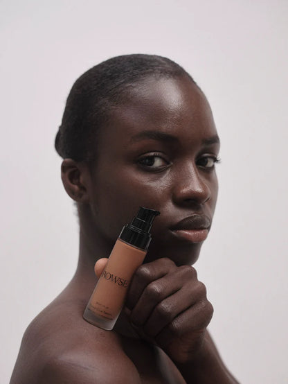 Woman holding a bottle of foundation against a plain background