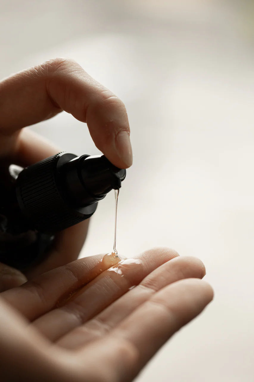 Hand holding a black bottle with serum dripping onto a palm against a neutral background