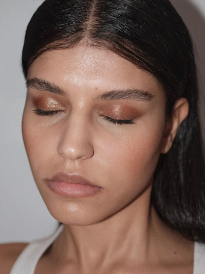 Close-up of a person with bronze makeup and dark hair against a plain background