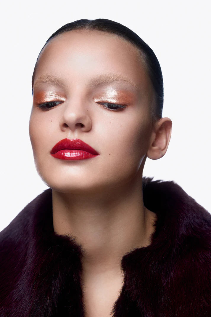 Woman wearing a dark fur coat with a plain background with bronze eyeshadow and red lip