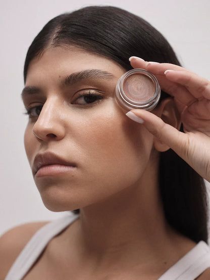 Woman holding a small round container near her face against a plain background