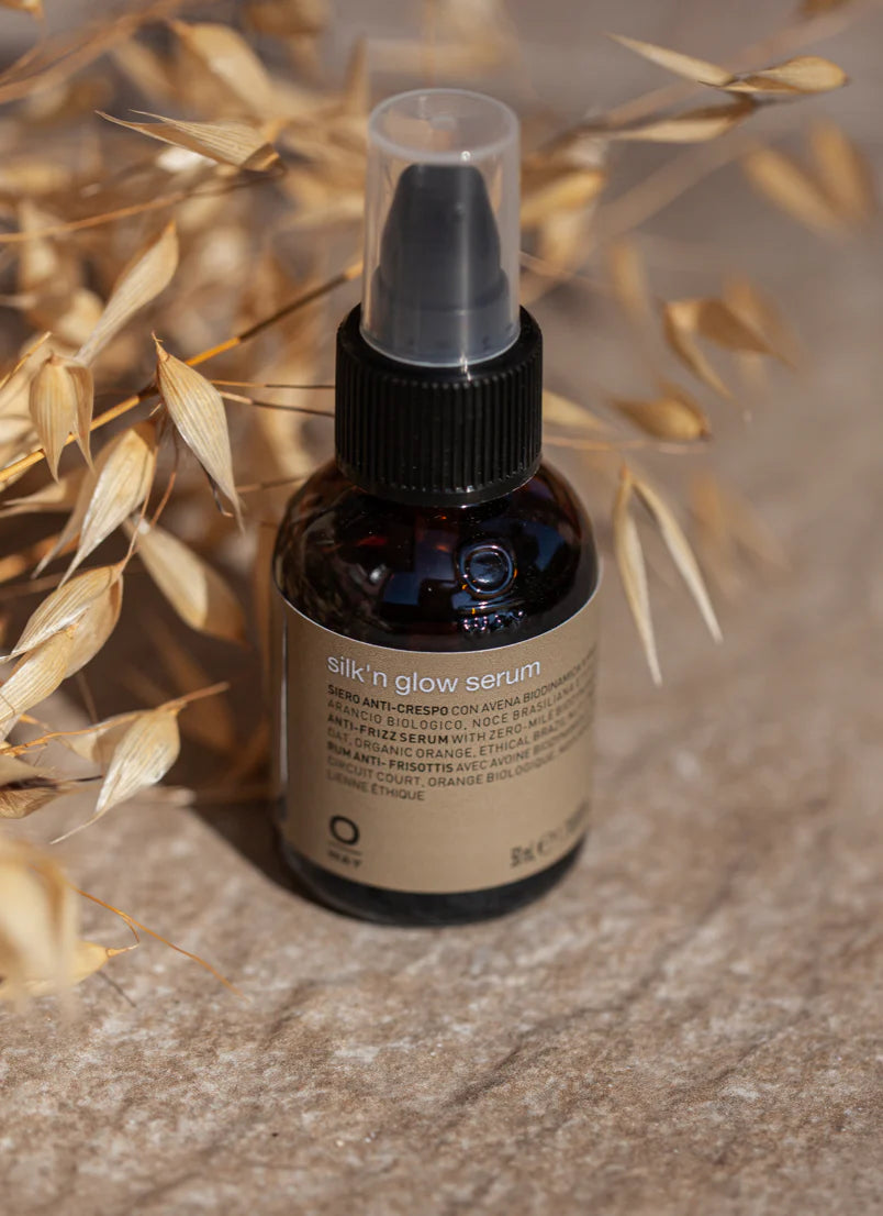 Bottle of silk 'n glow serum by OWAY on a textured surface with dried leaves.