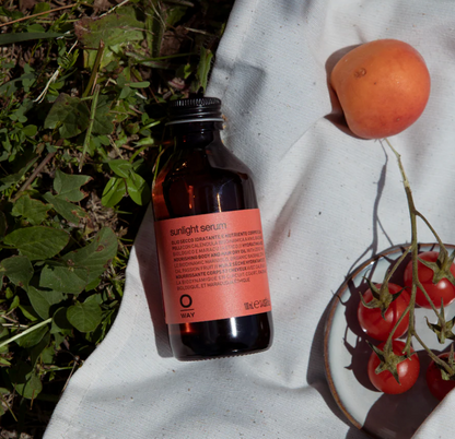Sunlight serum bottle with an apricot and tomatoes on a white linen cloth next to some greenery