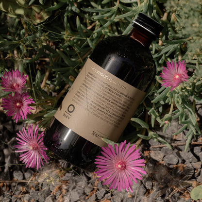 Bottle of 'Oway' hair oil on a natural background with pink flowers and green leaves.