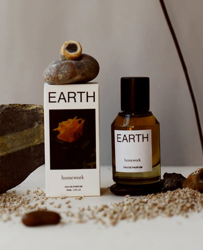 Earth-themed perfume bottle and packaging on a neutral background with rocks and seeds.