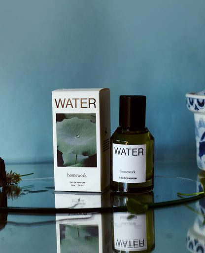 Perfume bottle and packaging labeled 'WATER' on a reflective surface with a blue background.