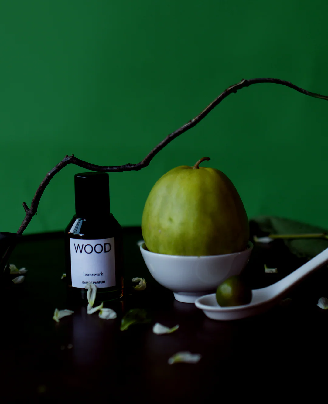Bottle labeled 'WOOD' with a green fruit and branch on a dark surface against a green background