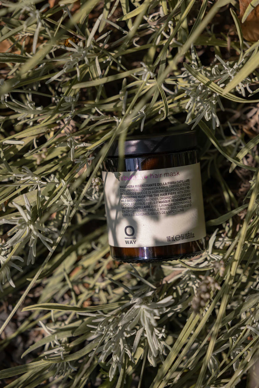 Jar RebuildM+ hair mask by OWAY on a bed of green leaves
