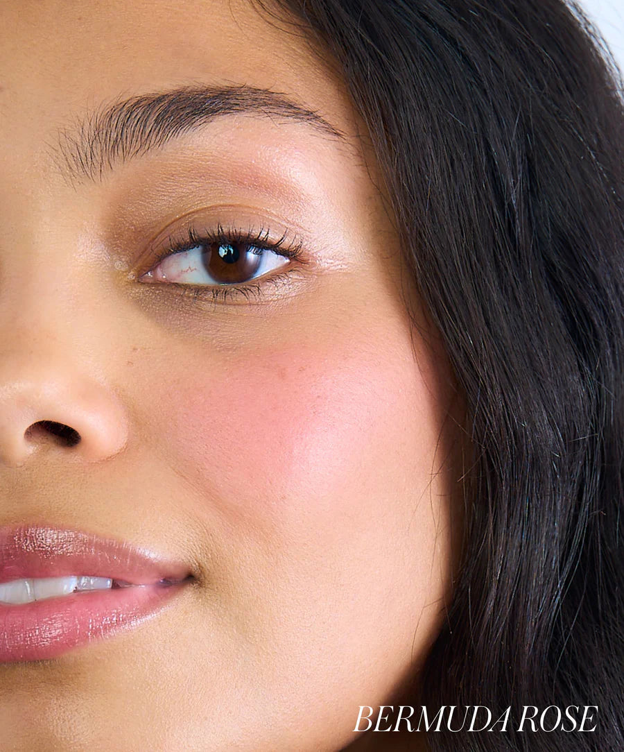 Close-up of a person's face with visible makeup, including blush, on a neutral background.
