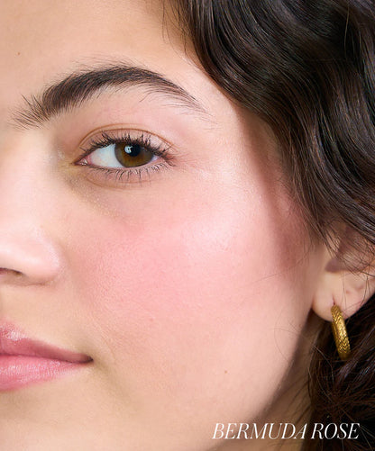 Close-up of a person wearing a gold hoop earring with 'Bermuda Rose' branding.