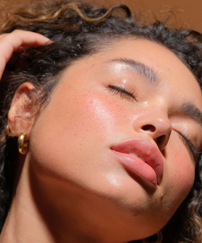 Close-up model shot showcasing RMS Beauty cream Luminizer applied to cheekbones, eyelids, and nose for a natural dewy finish