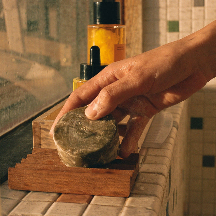 A hand placing a lathered up shampoo bar on a tiled ledge
