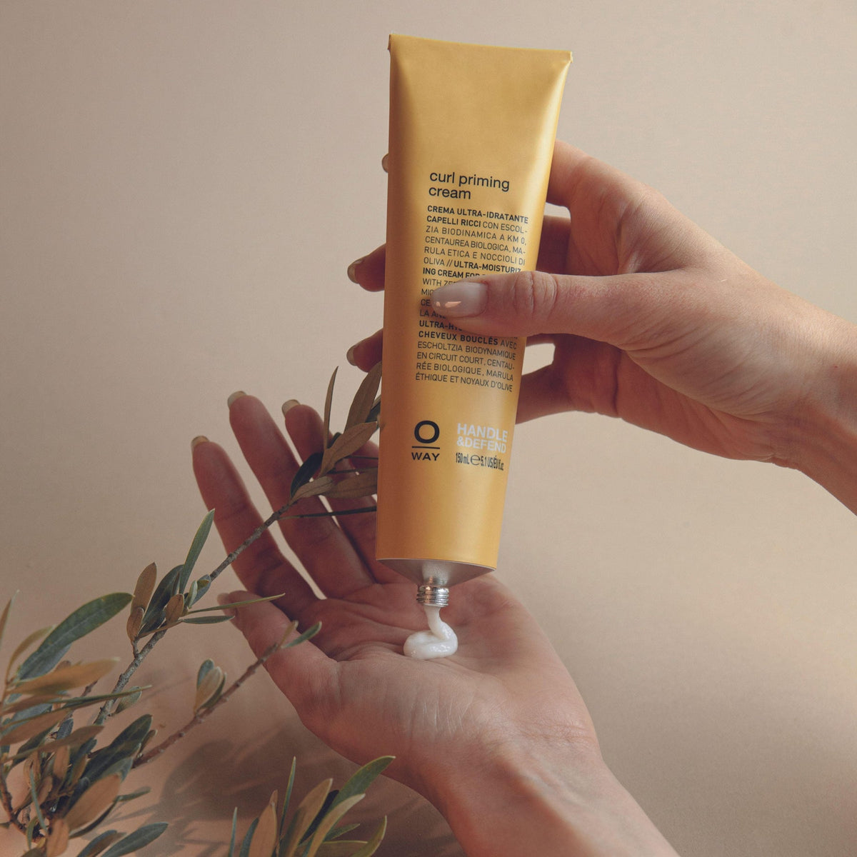 Yellow tube of OWAY curl priming cream held by two hands squeezing out the product ready for hair styling curly hair
